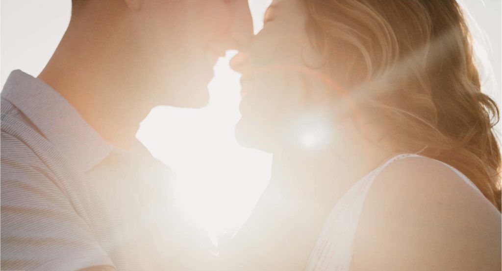 まぶしく光る太陽を背景に笑顔でキスしようとしているカップルの写真