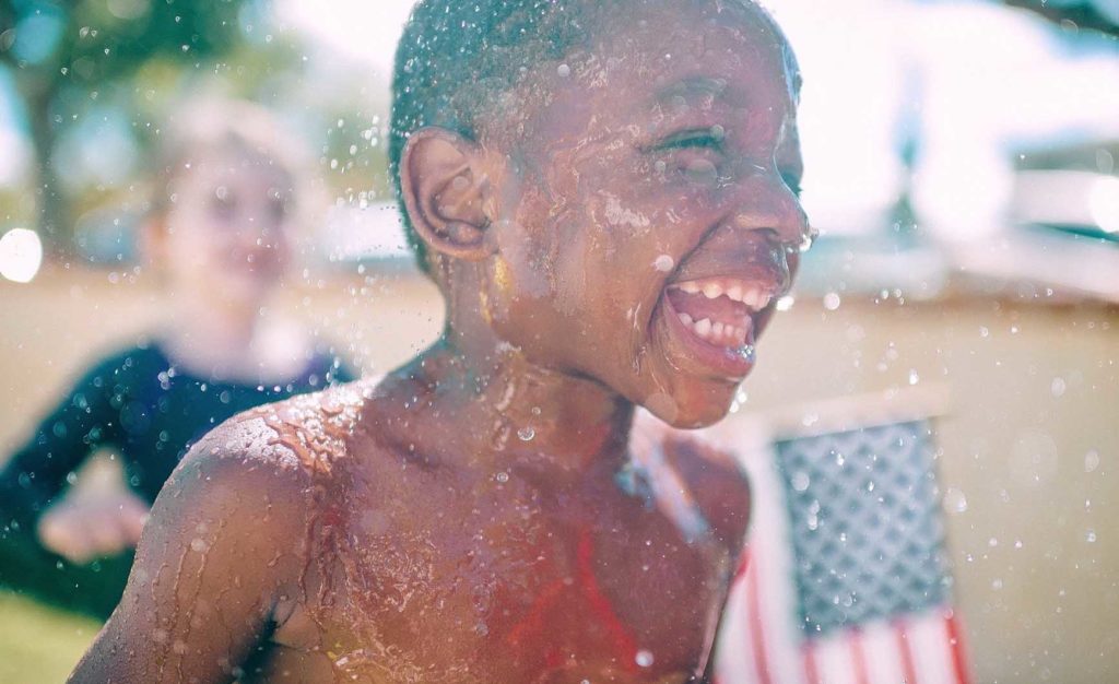 水遊びをして笑顔の黒人少年と後ろでアメリカ国旗を持って微笑んでいる白人の女の子の写真