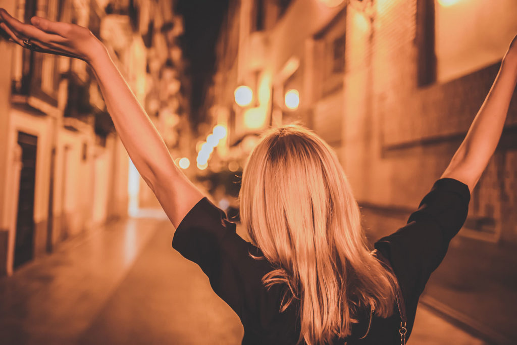 夜の街で楽しそうに両手を上げて歩いている女性の後ろ姿の写真
