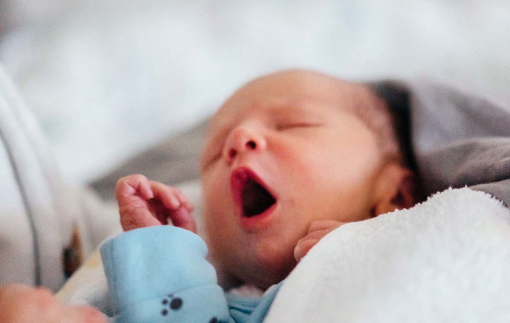 目をつぶったままあくびをする新生児の写真