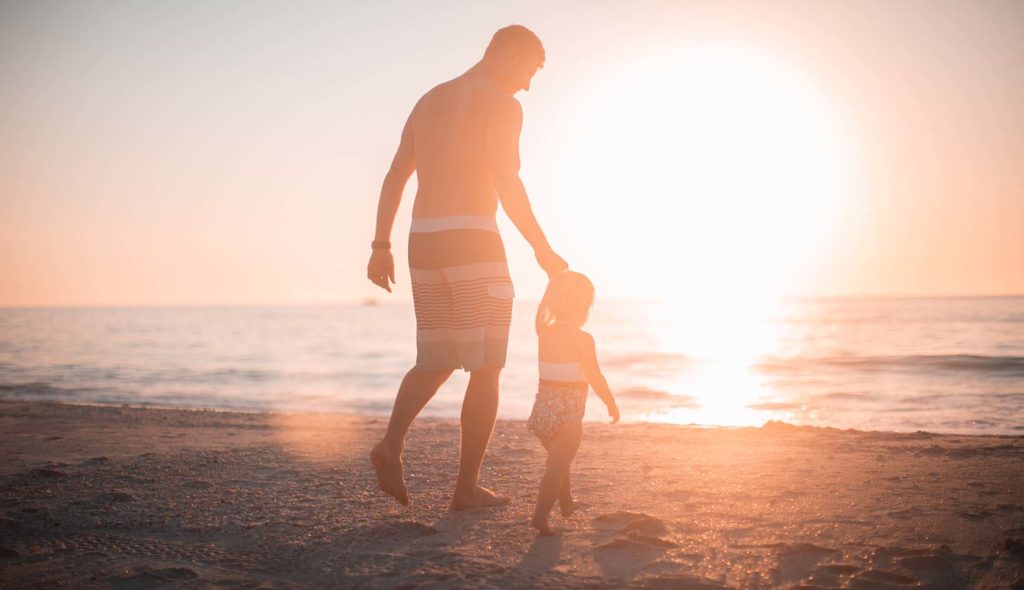 娘と手を繋ぎ夕日の海に向かう父の写真