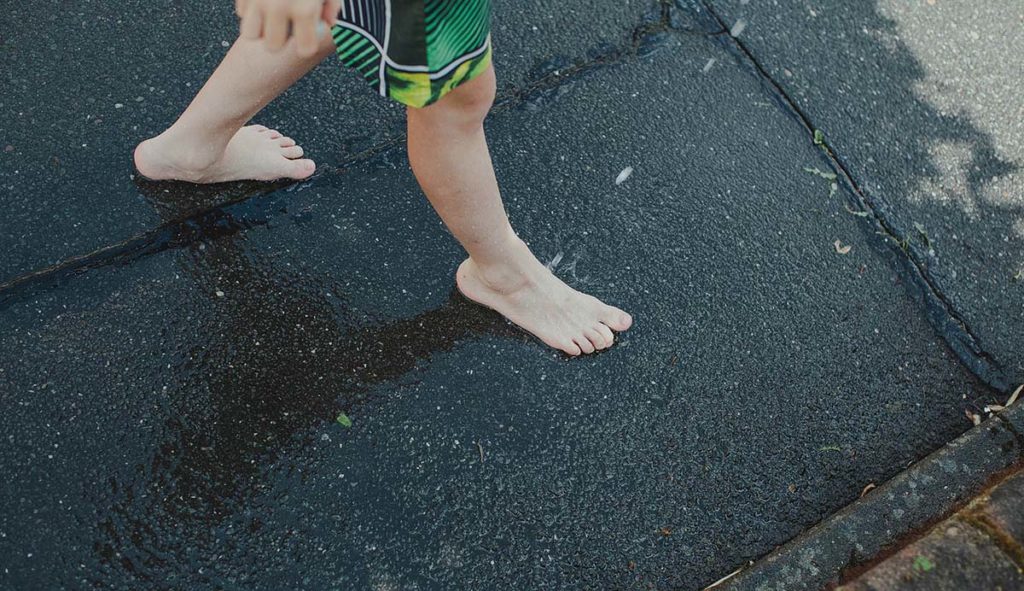 裸足でアスファルトの上を歩く少年の足元の写真