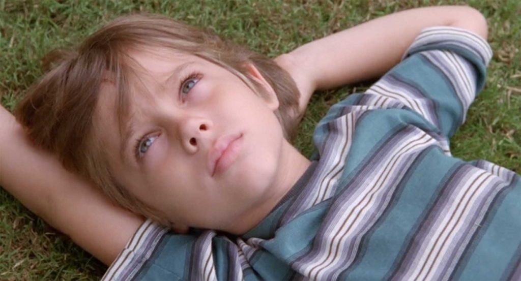 芝生に寝転がって空を見つめる少年「ボク」