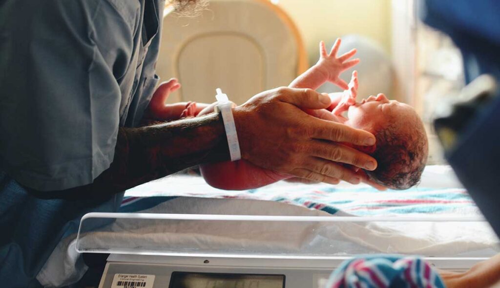 生まれた新生児を抱き上げる医師の手